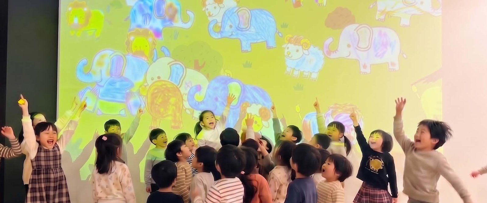 投影されたぬりえに手を伸ばして喜ぶ子どもたち