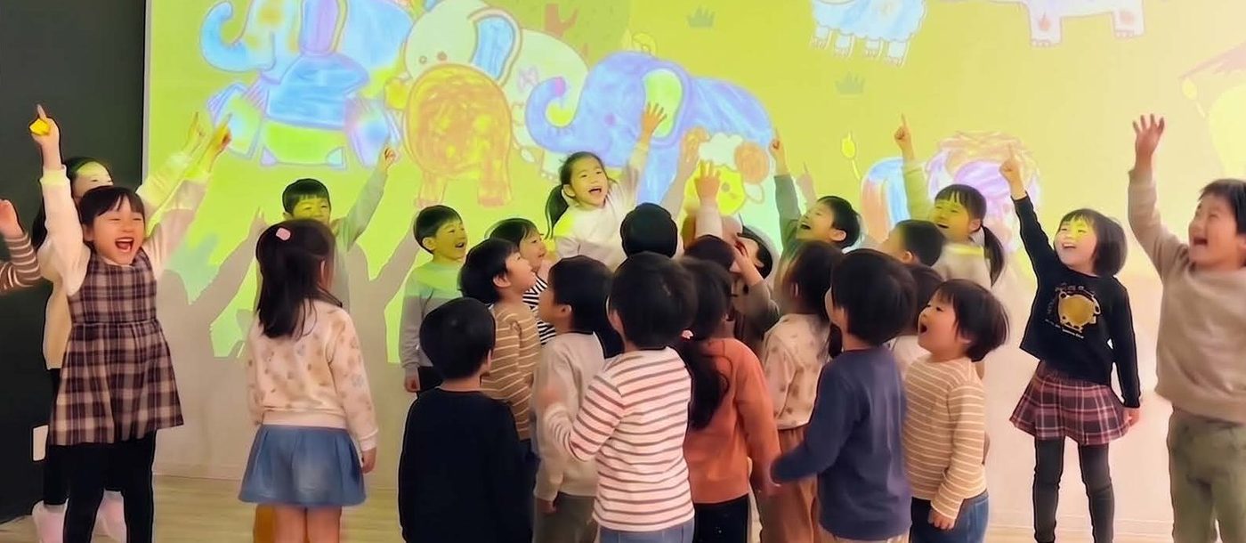 投影された象のぬりえに手を挙げて喜ぶ子どもたち